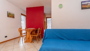 A room with a blue sofa, wooden dining table with chairs, a red partition, and a clock on the wall. - Casa Stella 8 (Falcade)