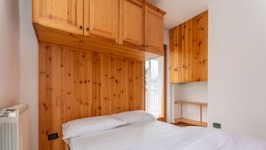 A bedroom with a wooden wardrobe, a bed with white bedding, and a radiator. - Casa Stella 8 (Falcade)