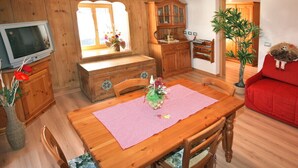 A wooden dining room with a table, chairs, a television, and a red sofa. - Casa Lisa (Falcade)
