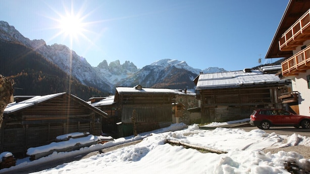 A snowy mountain village with wooden houses and a red car parked on the street. - Casa Lisa (Falcade)