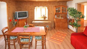 A wooden dining area with a table, chairs, a television, and a cabinet. - Casa Lisa (Falcade)