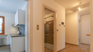 A modern kitchen with a built-in oven, a sink, and a window. A glass shower is visible through an open door. - Casa Zulian (Falcade)