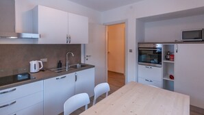 A compact kitchen with white cabinets, a stainless steel sink, a microwave, and a wooden table. - Casa Zulian (Falcade)