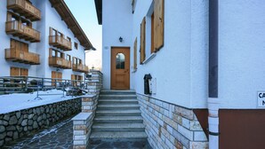 A narrow stone staircase leading to a wooden door, flanked by buildings with wooden balconies and a stone wall on one side. - Casa Zulian (Falcade)