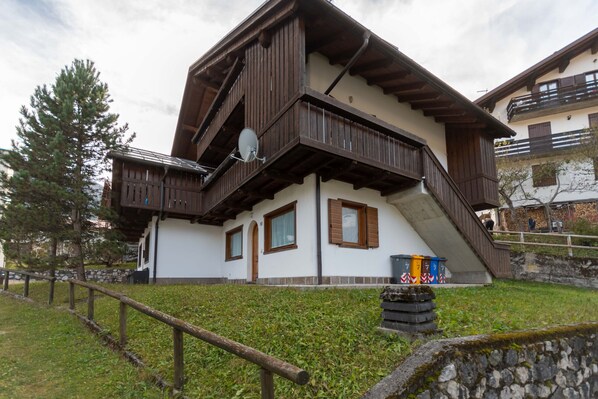 A traditional chalet with a wooden balcony, a satellite dish, and a stone wall.