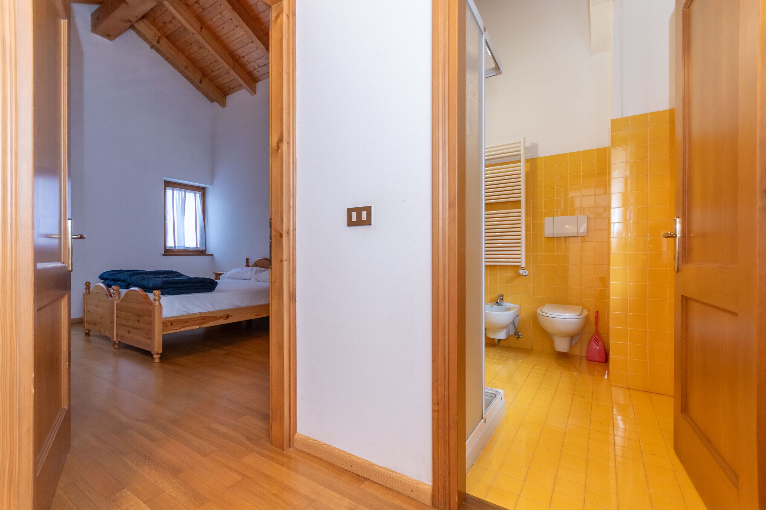 A bedroom with a wooden bed, a window, and a bathroom with a toilet and sink.