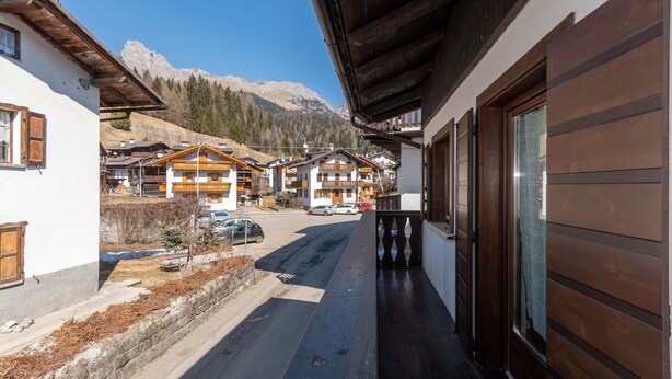 Un village de montagne aux maisons traditionnelles en bois, sous un ciel dégagé, avec une route qui mène à la montagne.