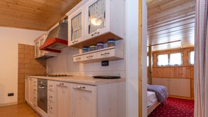 A compact kitchen with wooden cabinets, a built-in oven, and a red patterned carpet in the adjacent room.