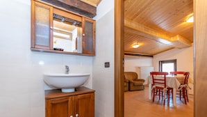 A bathroom with a wooden cabinet, a large sink, and a mirror. There is a dining area with a table and chairs in the background.
