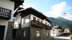 A traditional stone building with a balcony, a street in front, and a mountain in the background.