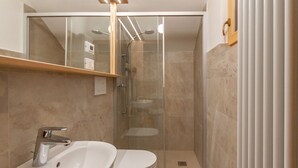Ein modernes Badezimmer mit einer gläsernen Duschkabine, einem weißen Waschbecken und einem Spiegel darüber.