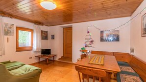 A cozy room with wooden floors, a dining table with benches, a green sofa, and a television. - Casa Morel (Falcade)
