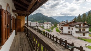 A wooden balcony with a view of a mountain village, featuring traditional buildings and a paved street. - Casa Morel (Falcade)