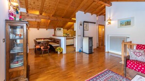 A spacious living area with wooden flooring, a dining table, and a kitchen in the background. - Casa Fagher (Falcade)