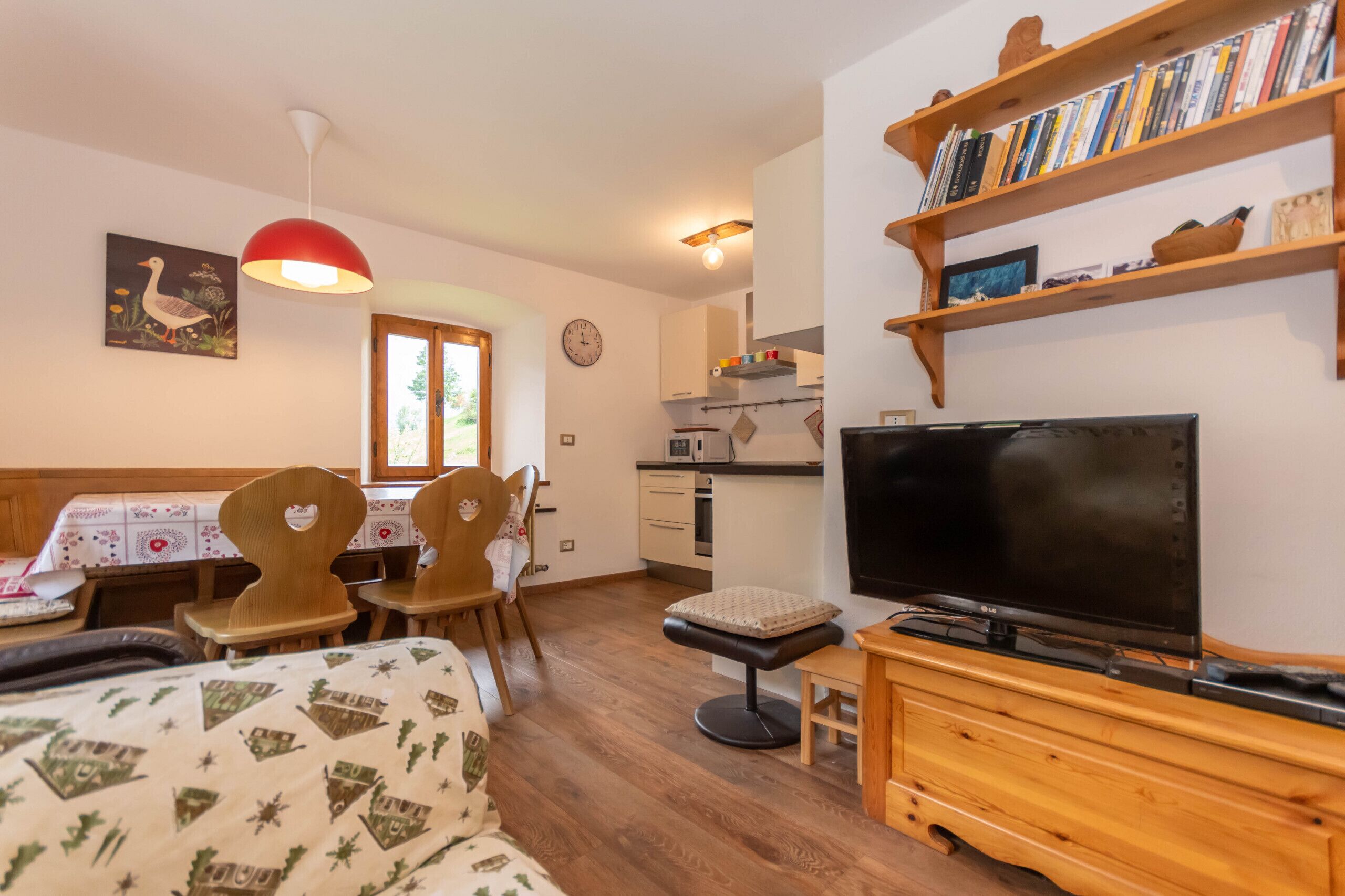 Una sala de estar acogedora con televisor, muebles de madera, una estantería y un comedor con mesa y sillas.