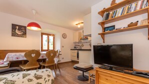 Uma sala de estar aconchegante com televisão, móveis de madeira, uma estante de livros e um espaço de jantar com mesa e cadeiras.