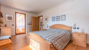 Ein Schlafzimmer mit einem hölzernen Bett, einem Nachttisch, einem Sessel und einer Tür, die auf einen Balkon führt.