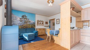 Ein gemütliches Wohnzimmer mit einem blauen Sofa, einem Holzespeisetisch mit Stühlen und einer Küchenzeile mit Holzschränken.