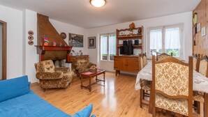 A cozy living room with a blue sofa, patterned armchairs, a wooden coffee table, and a dining area with a table and chairs. - Villa Elisena (Falcade)