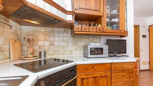 A kitchen with wooden cabinets, a microwave, a stove, and a toaster. - Casa Alice (Falcade)