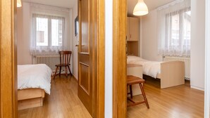 A bedroom with two beds, a wooden wardrobe, a chair, and a radiator. - Casa Alice (Falcade)