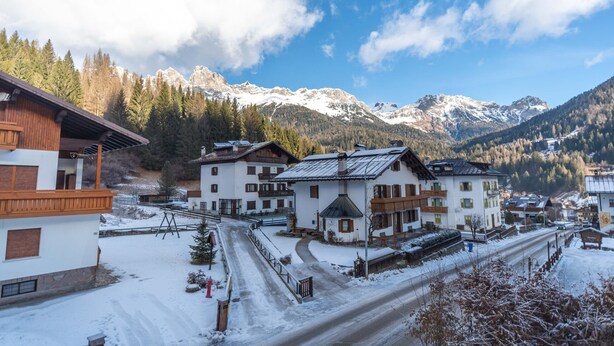 Ein verschneites Dorf mit traditionellen Holzbauten, einem klaren Himmel und schneebedeckten Bergen im Hintergrund.