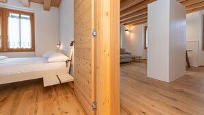 Ein Schlafzimmer mit Holzboden, einem Bett, einem Kleiderschrank und einem Fenster mit Vorhängen.