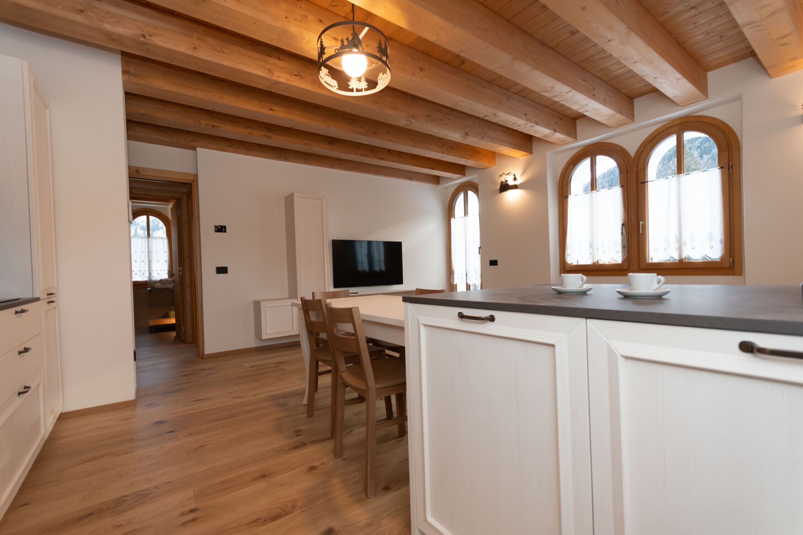 A spacious kitchen with wooden beams, a dining area with chairs, and a TV.