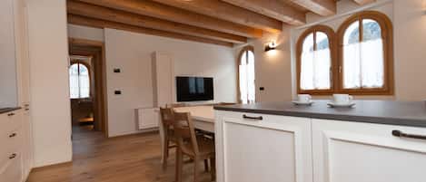 A spacious kitchen with wooden beams, a dining area with chairs, and a TV.