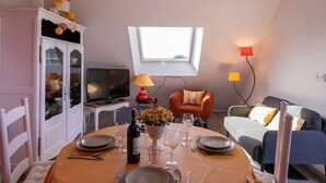 Un coin repas avec une table dressée pour deux personnes, un téléviseur et un meuble avec des portes en verre.