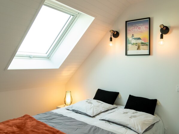Ein Schlafzimmer mit Dachfenster, einem Bett mit zwei Kissen, einem Nachttisch mit Lampe sowie einem gerahmten Bild an der Wand.