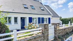 Une maison blanche avec des volets bleus, un mur de pierre et une clôture blanche.