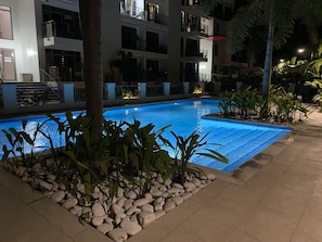 A swimming pool surrounded by rocks and plants, with a building in the background.