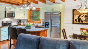 A modern kitchen with wooden beams, a stainless steel refrigerator, and a dining area with a sofa and chairs. - "Lil Cub" Cabin in Nebo Gated Community (Nebo)