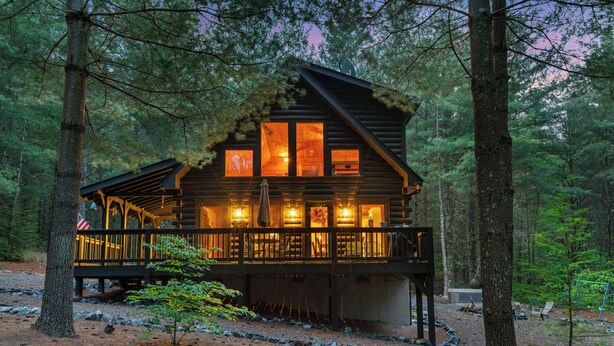 A log cabin with a deck and multiple windows, surrounded by a forest. - "Lil Cub" Cabin in Nebo Gated Community (Nebo)