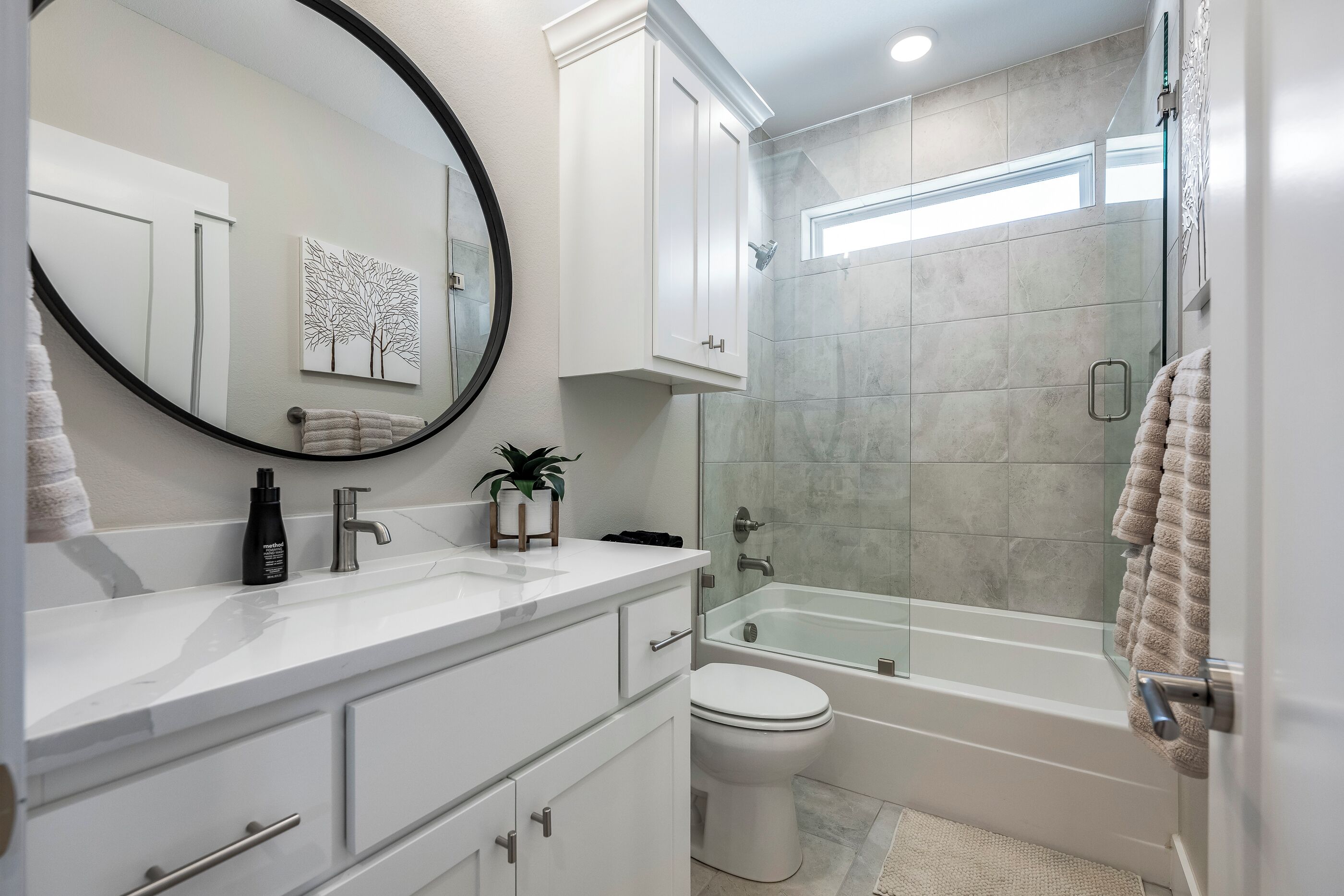 Une salle de bain moderne avec un meuble-lavabo blanc, un miroir rond, des toilettes et une douche à parois de verre.