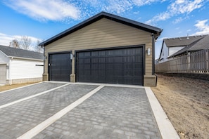 A two-car garage attached to a building with a brick driveway and a wooden fence.