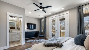 A bedroom with a bed, a ceiling fan, a TV, and a view of the outdoors. - New luxurious home - hot tub, firepit, & trails - Walk or ride to downtown! (Bentonville)