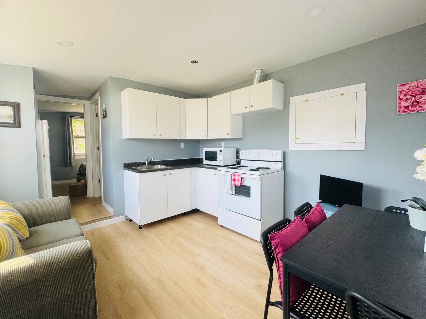 A compact kitchen with white cabinets, a microwave, and a stove. There is a dining area with a table and chairs.