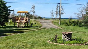 A wooden cabin with a thatched roof, a dirt path leading to it, and a stone structure nearby. - Pine Cottages (Stanhope)