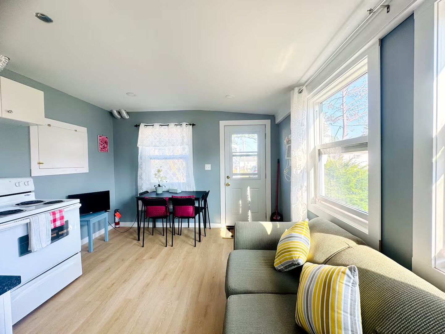A compact living space with a kitchenette, dining area, and a sofa with cushions.