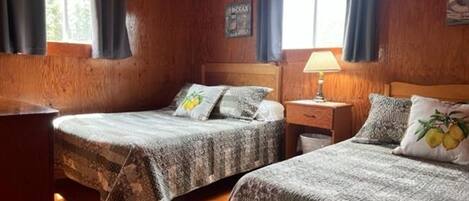A cozy cabin-style room with two beds, wooden walls, and a window with curtains.