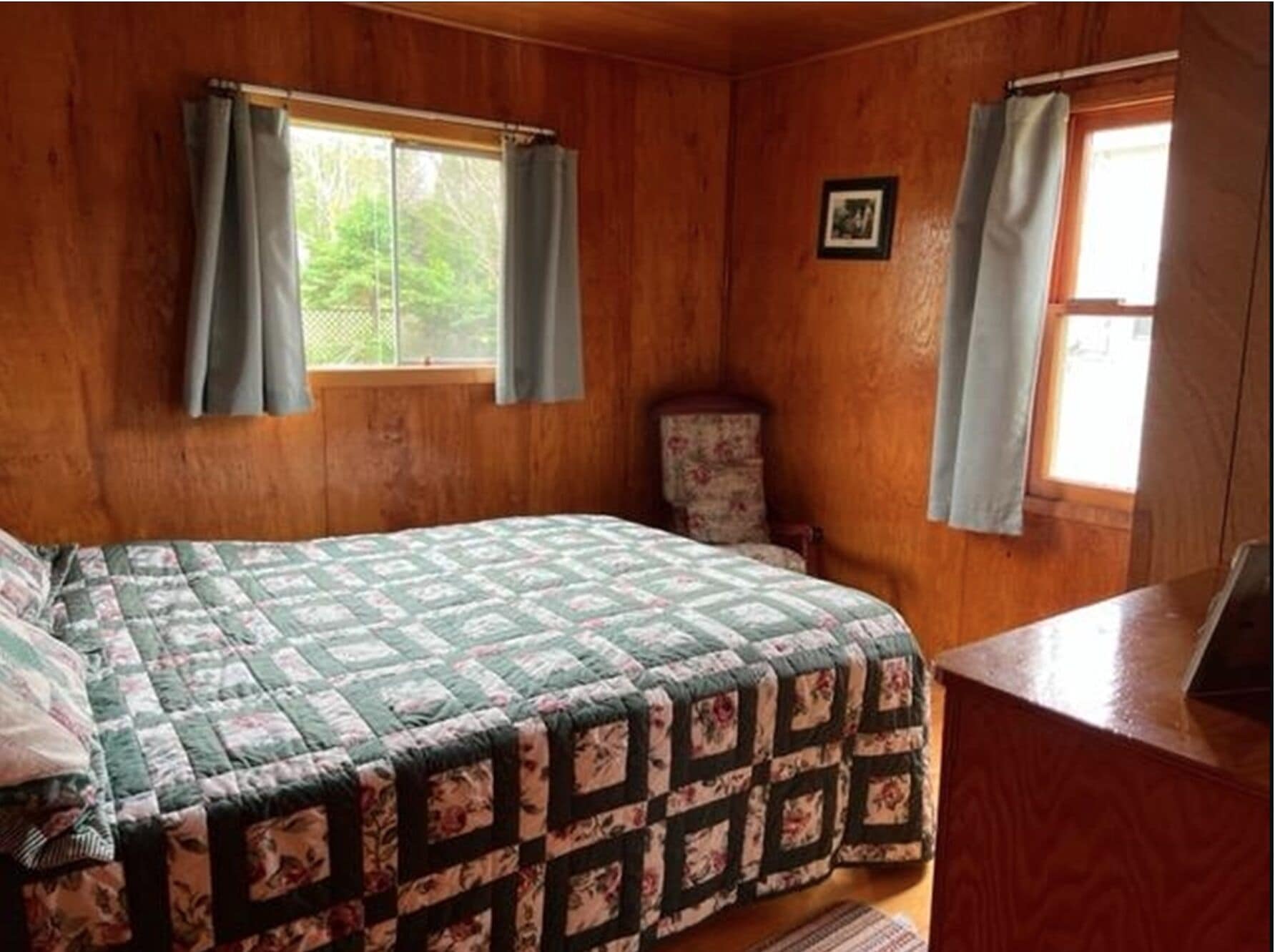 A wooden cabin room with a bed, a chair, and a desk.