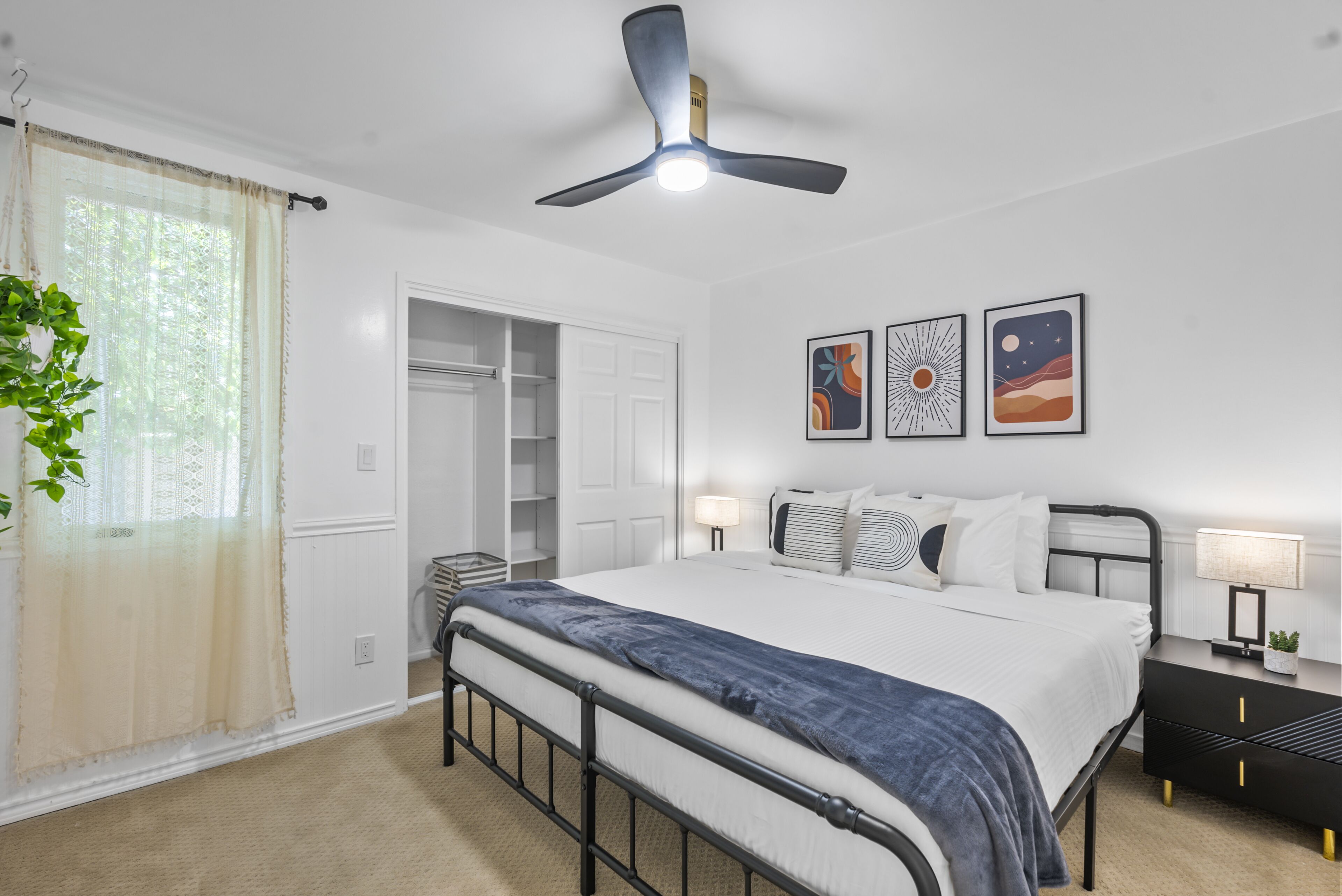 Un dormitorio con cama, mesitas de noche, ventilador de techo, armario y obras de arte en la pared.