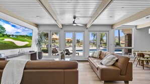 Un salon spacieux doté d’un grand téléviseur, de canapés en cuir et offrant une vue sur un terrain de golf et une piscine.