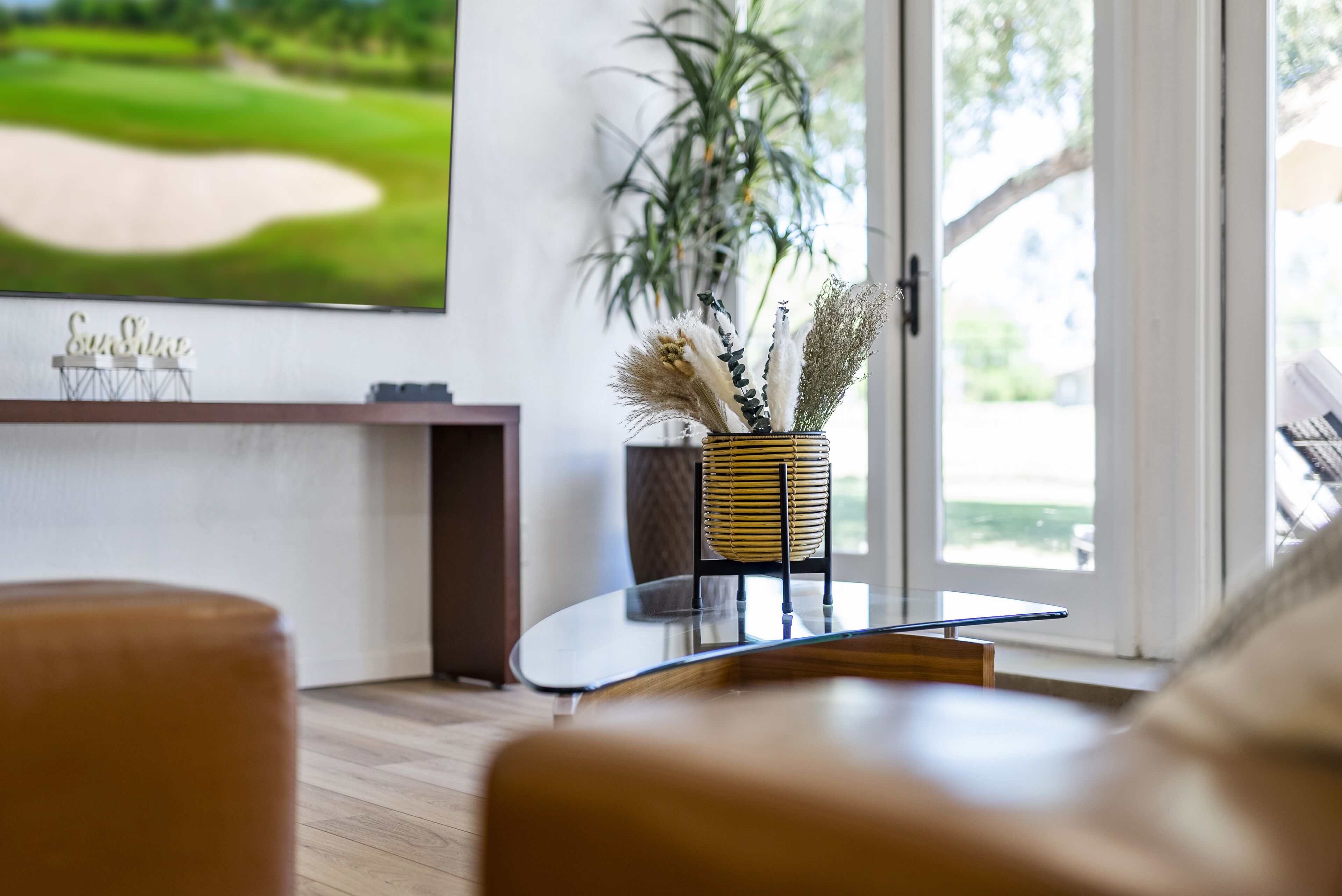 A modern living room with a glass coffee table, a potted plant, and a television displaying a golf course.