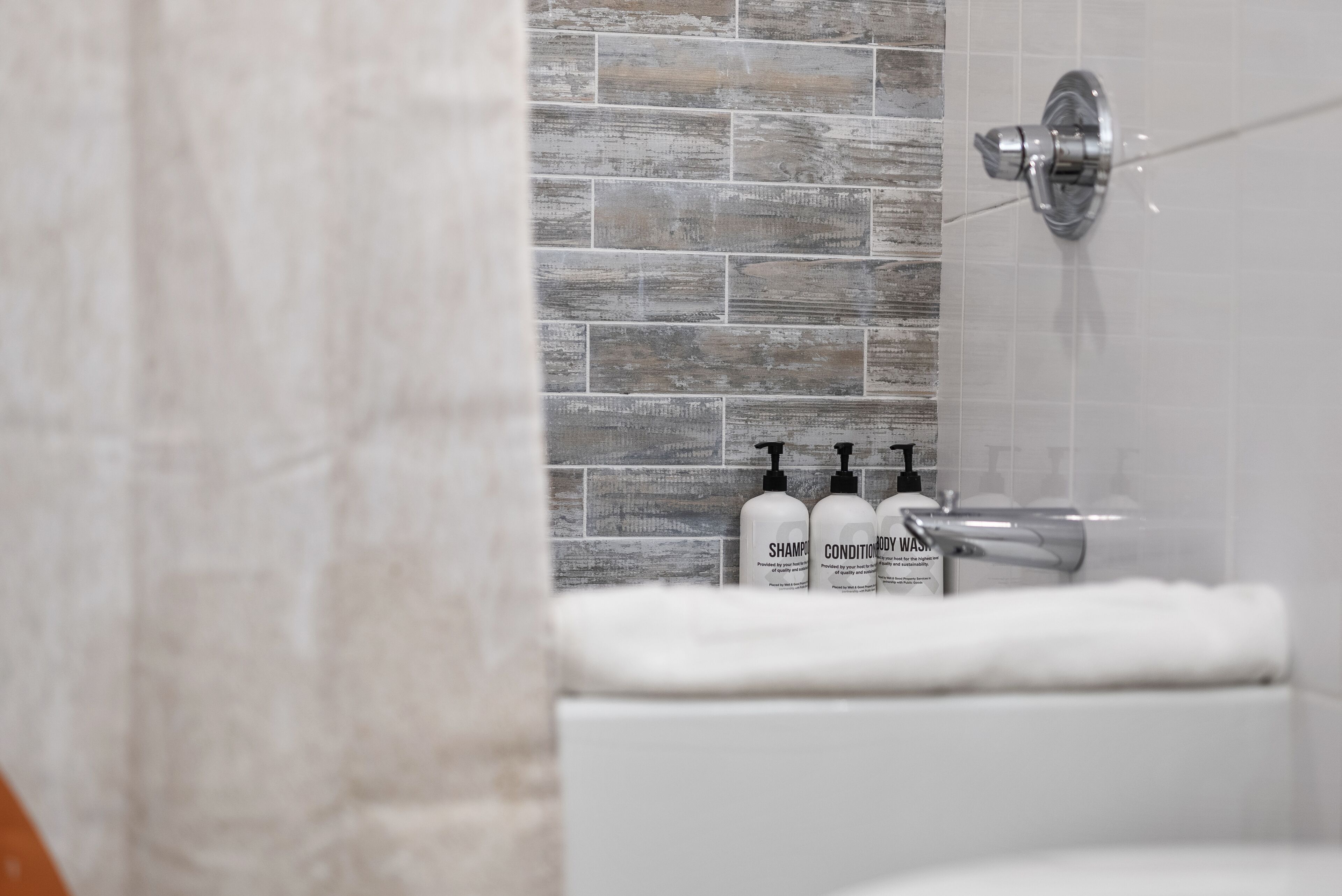 A bathroom with a shower, a white bathtub, and three bottles of shampoo and conditioner on the wall.
