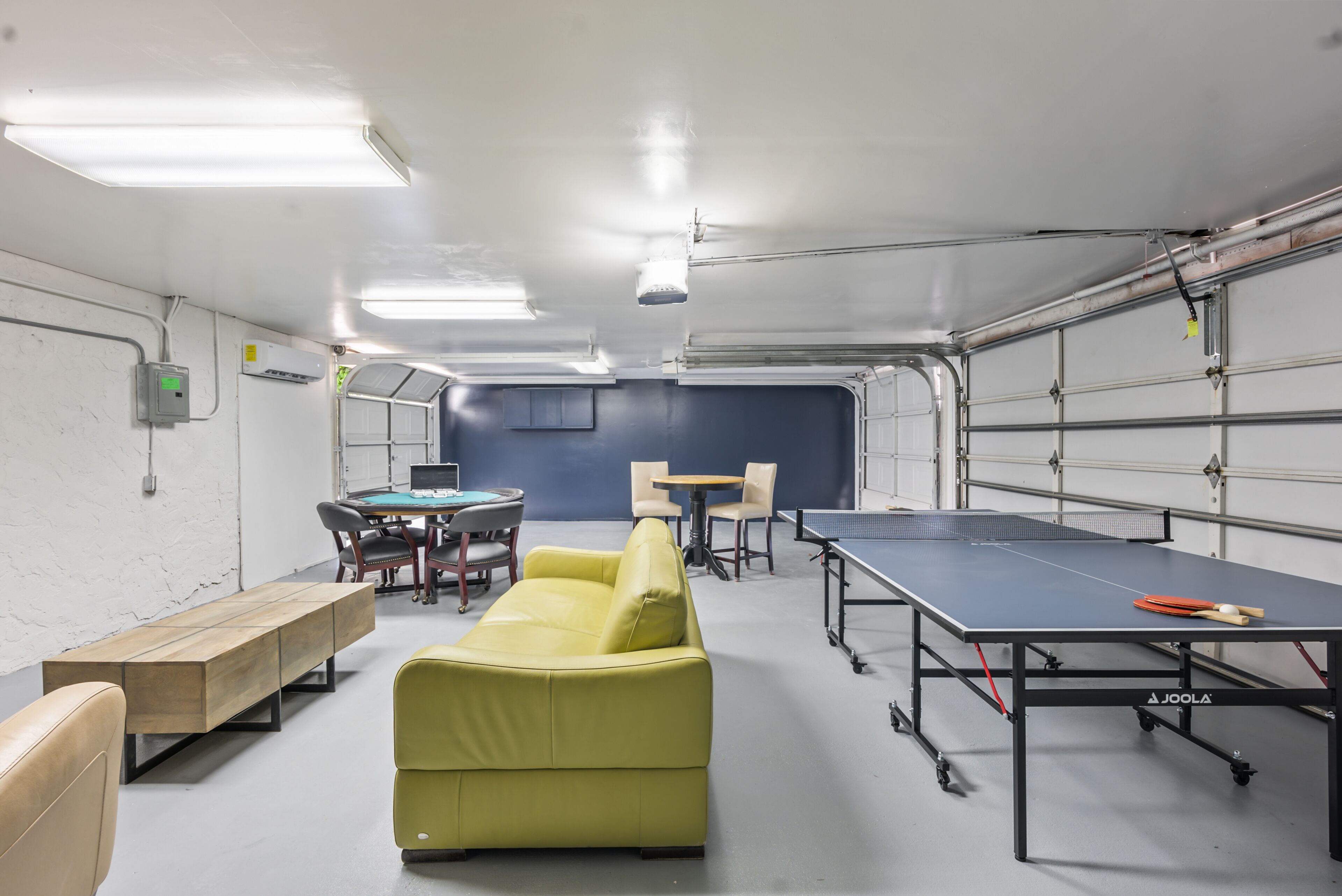 Ein Raum mit einem Pongtisch, einem gelben Sofa, einer Holzbank und einem Tisch mit Stühlen.