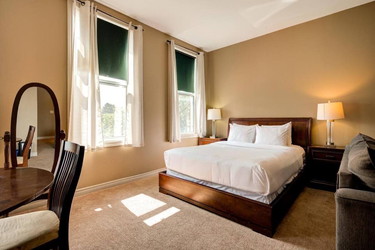 A bedroom with a large bed, two bedside lamps, a chair, a table, and a mirror.