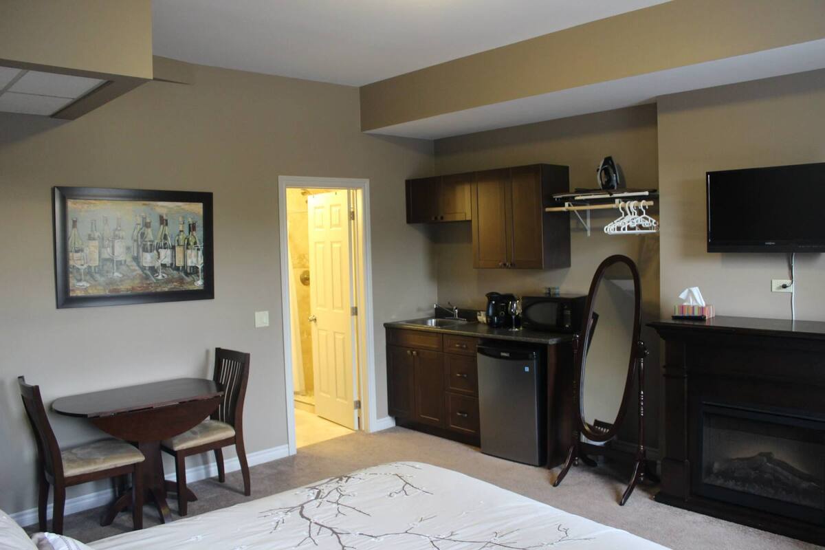 A hotel room with a dining table, chairs, a kitchen area, a fireplace, and a television.